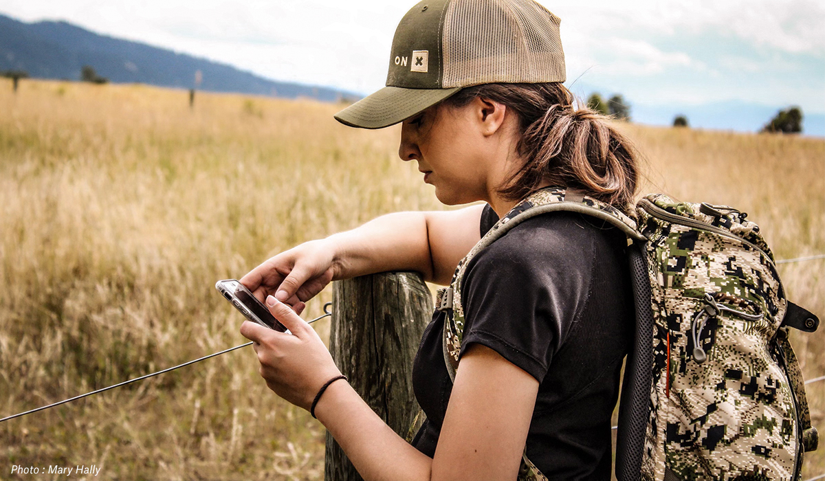 Woman looking at phone while hunting and hiking beside fenceline. Woman looking at phone while hunting and hiking beside fenceline.