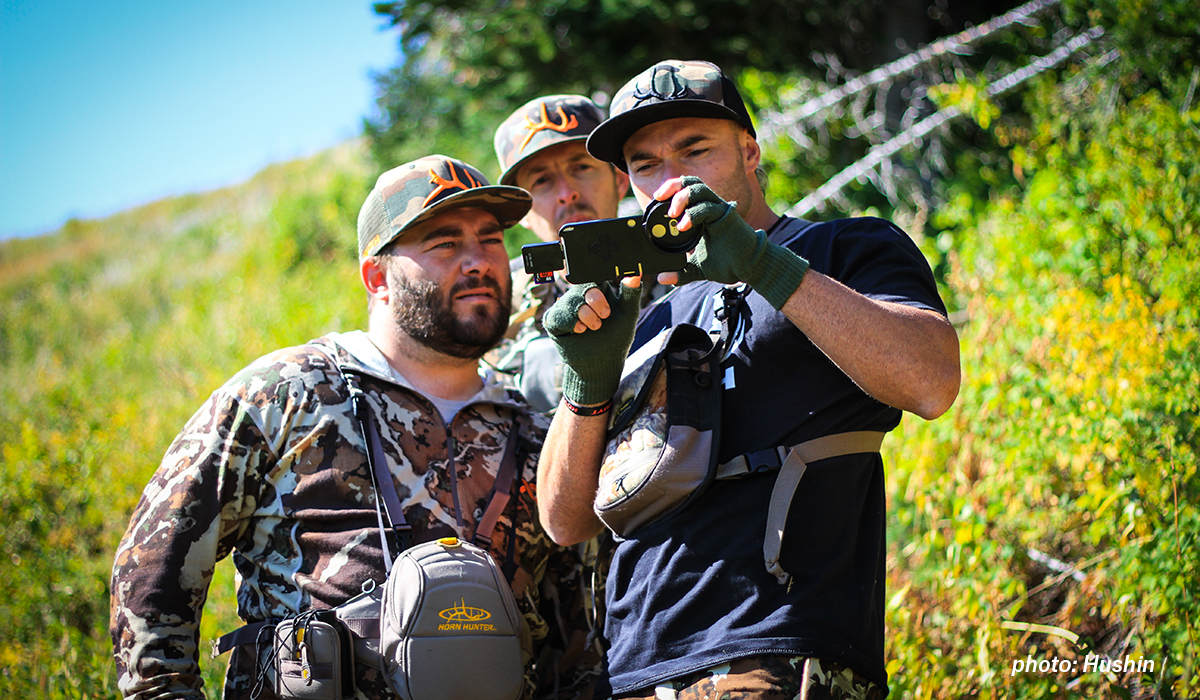 Three men gather around a phone while hunting. Three men gather around a phone while hunting.