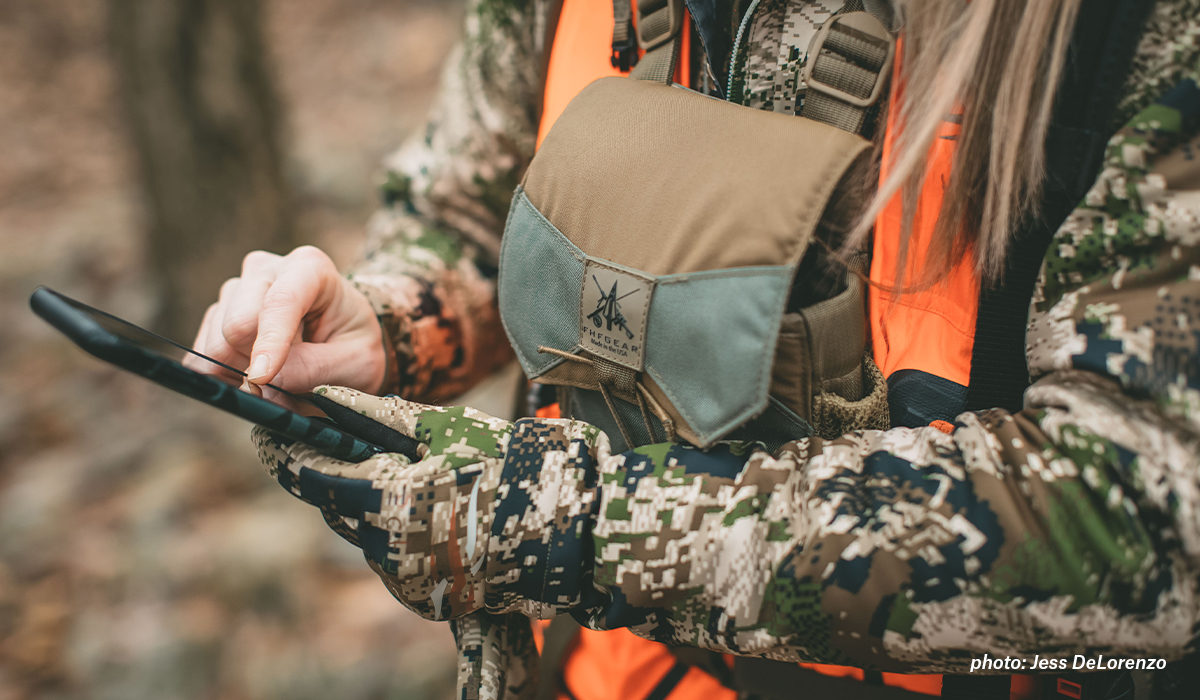 Woman hunting in camouflage looking at an app on her phone. Woman hunting in camouflage looking at an app on her phone.