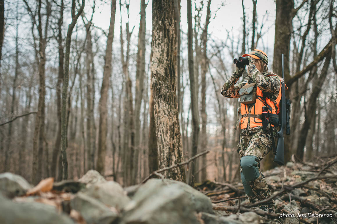 Woman looking through binoculars while hunting in the Northeast with a rifle. Woman looking through binoculars while hunting in the Northeast with a rifle.