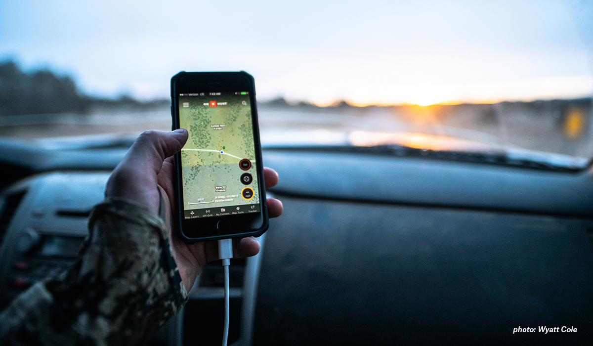 Man holding phone with onX Hunt App showing on screen in car. Man holding phone with onX Hunt App showing on screen in car.