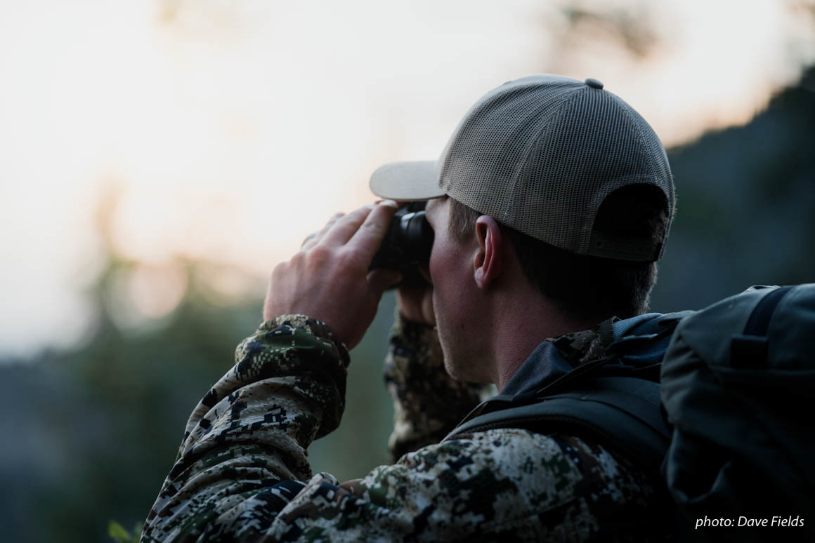 Man in camouflage uses binoculars to spot elk while hunting in the Montana backcountry. Man in camouflage uses binoculars to spot elk while hunting in the Montana backcountry.