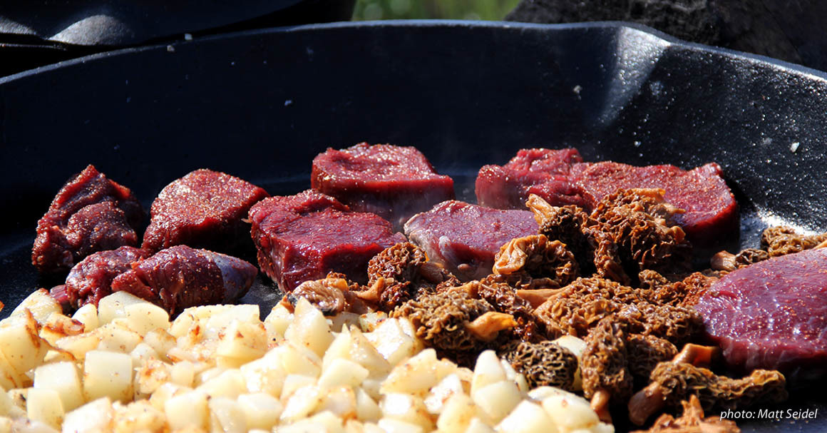 Game meat, morel mushrooms and potatoes in a large cast-iron skillet. Game meat, morel mushrooms and potatoes in a large cast-iron skillet.
