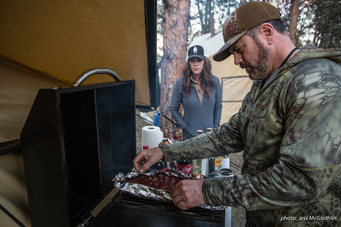 A man and woman cook food while in a wall tent camp hunting in Montana. A man and woman cook food while in a wall tent camp hunting in Montana.