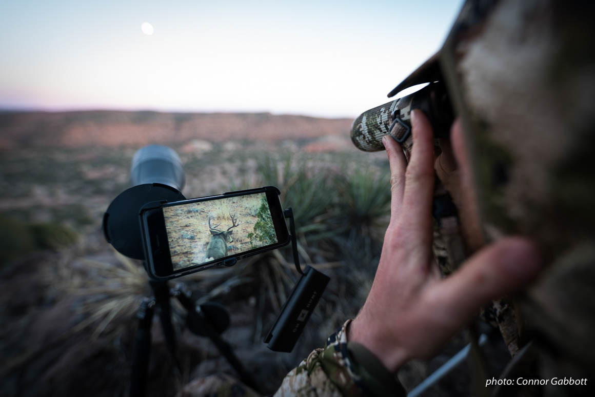 Man watches deer through phone scope while hunting in Arizona. Man watches deer through phone scope while hunting in Arizona.