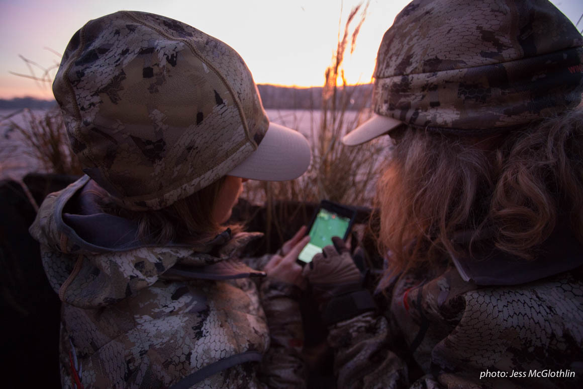 Two female hunters look at the onX Hunt App while in a goose blind at sunrise in New Jersey. Two female hunters look at the onX Hunt App while in a goose blind at sunrise in New Jersey.