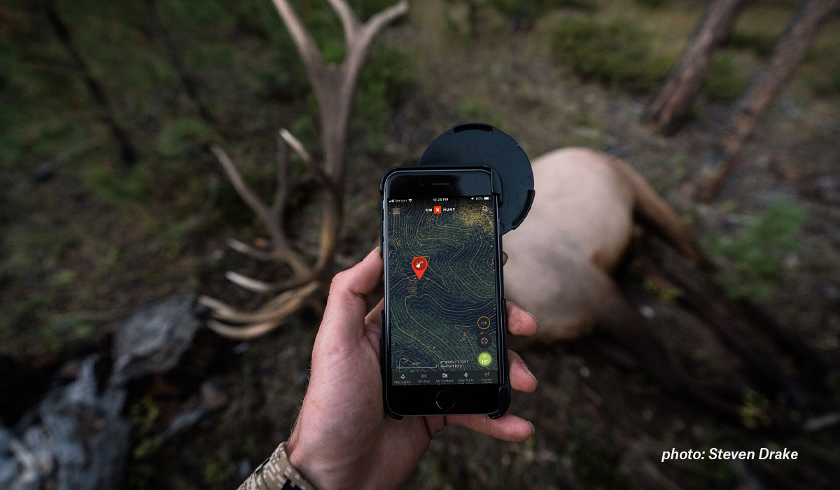 A hunter stands over an elk looking at onX Hunt with an elk Waypoint. A hunter stands over an elk looking at onX Hunt with an elk Waypoint.