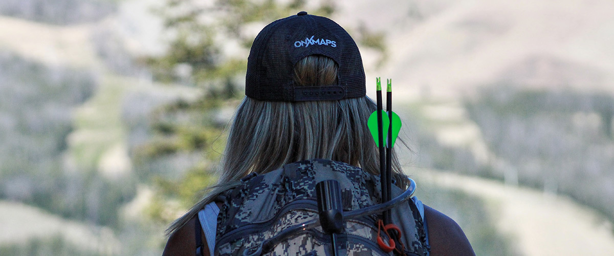 Female bowhunter with onX Hunt cap with camouflage backpack. Female bowhunter with onX Hunt cap with camouflage backpack.