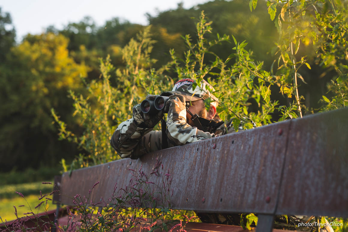Man with binoculars leaning over fence glassing while hunting. Man with binoculars leaning over fence glassing while hunting.