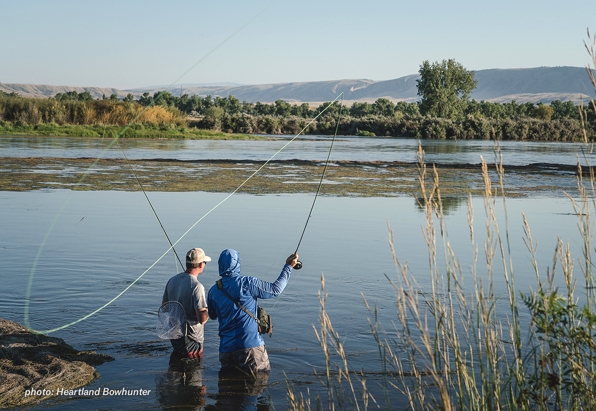 Two men fishing a river in the summertime with fly rods. Two men fishing a river in the summertime with fly rods.