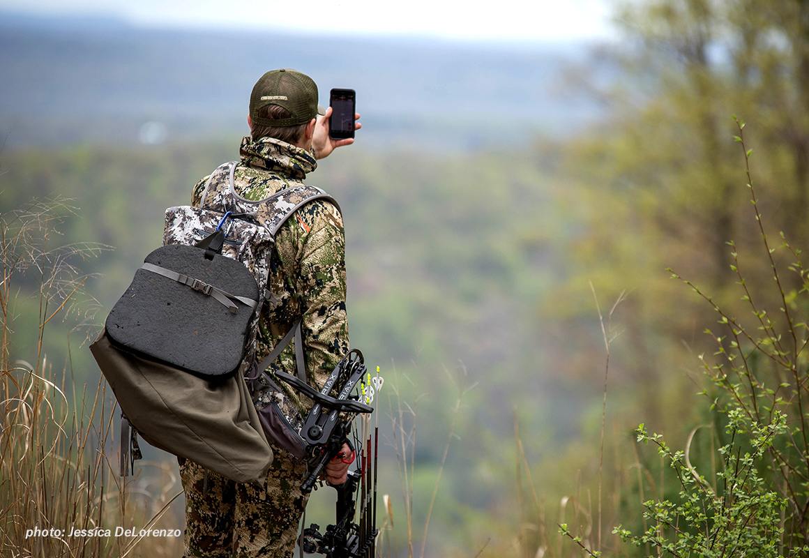 Bowhunter looking at the onX Hunt App in the backcountry Bowhunter looking at the onX Hunt App in the backcountry